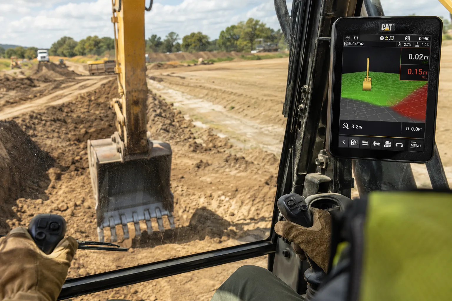 The view from an excavator cab, with a Cat grade control screen showing the design surface shaded green and red alongside live cut and fill readings, while the bucket trims a drain outside